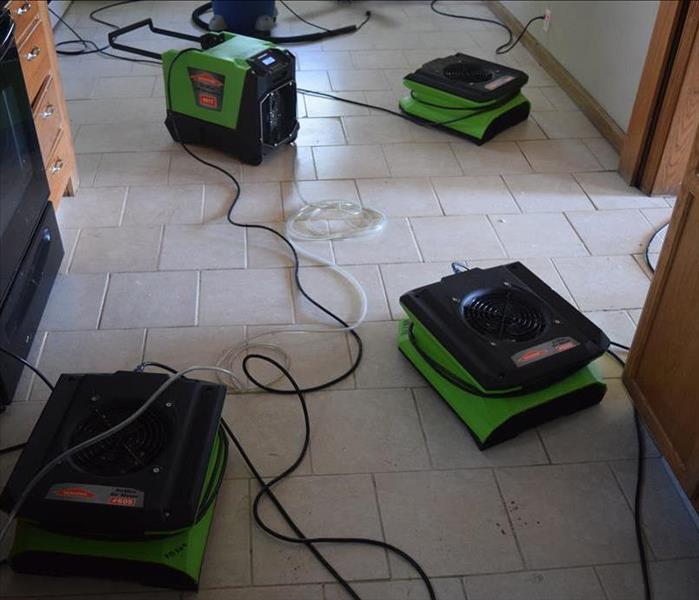 White tile floor in a kitchen with air movers and a dehumidifier placed strategically to dry the water