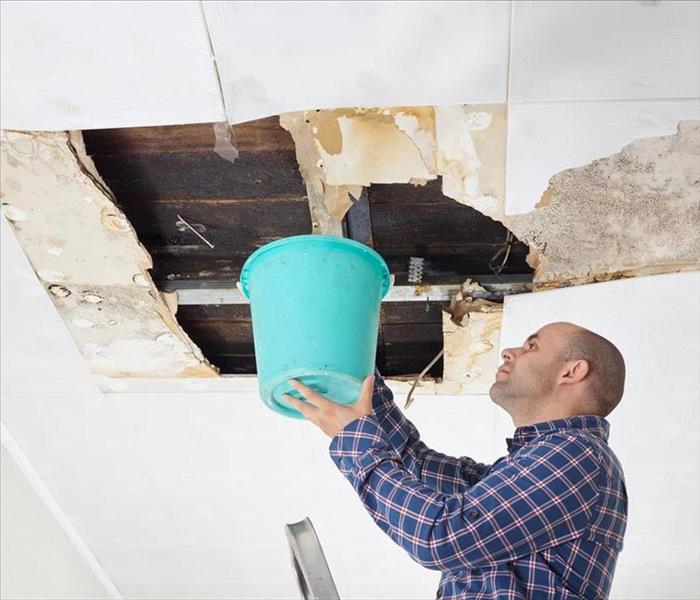 Man collecting water in bucket from ceiling