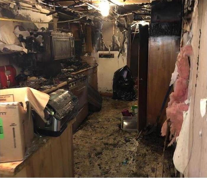 Severe fire damage in a kitchen, insulation coming out of walls, ceiling damaged and walls covered with smoke damage
